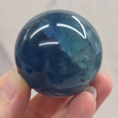 Blue Fluorite sphere being held in a hand against a white background