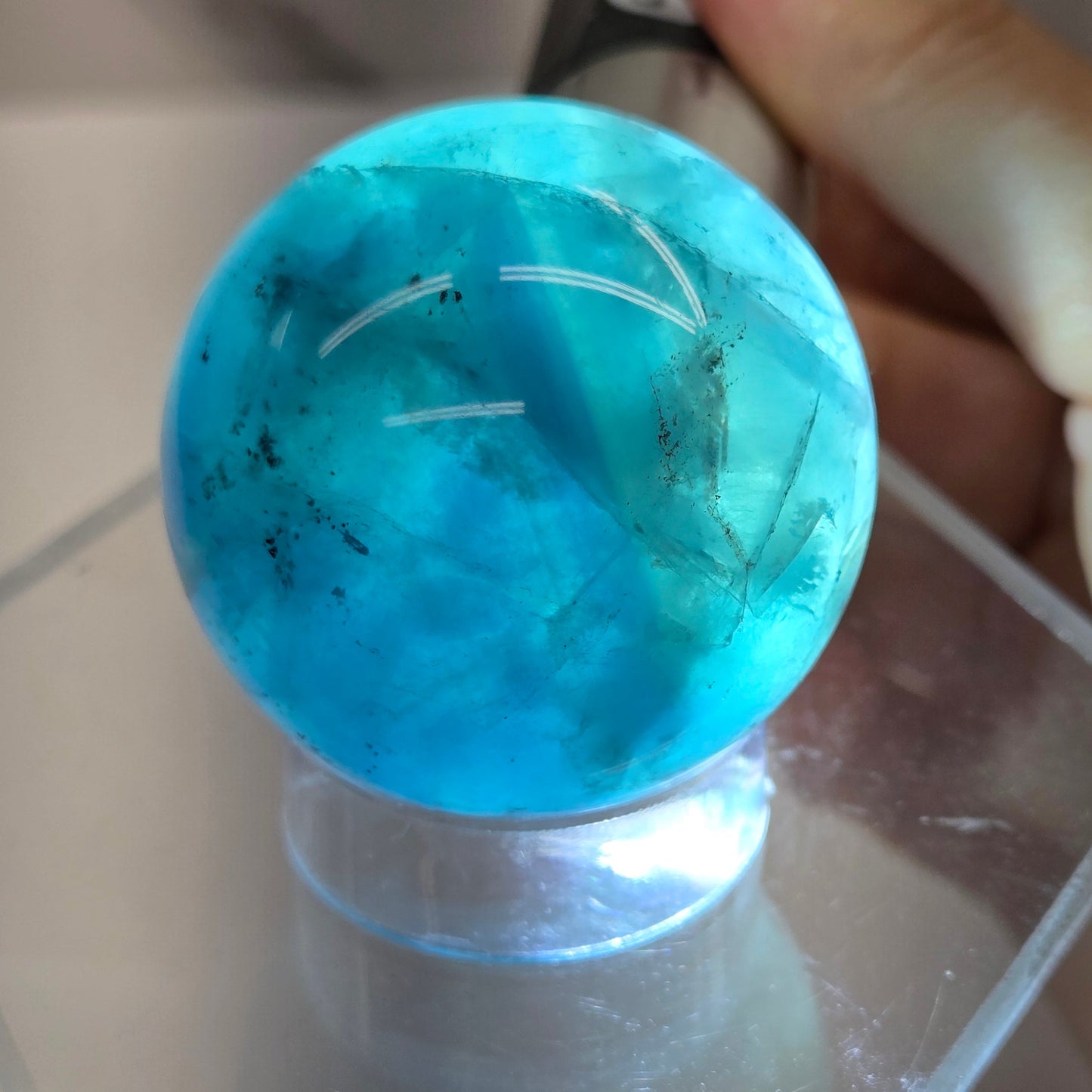 Backlit Blue Fluorite sphere on an acrylic stand against a white background