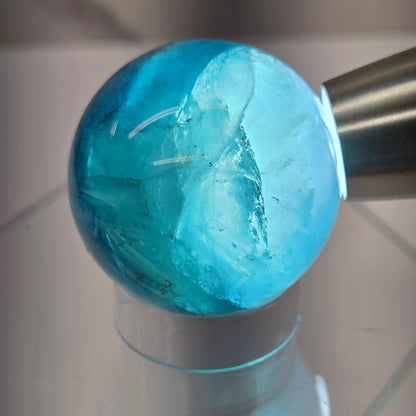 Backlit Blue Fluorite sphere on an acrylic stand against a white background