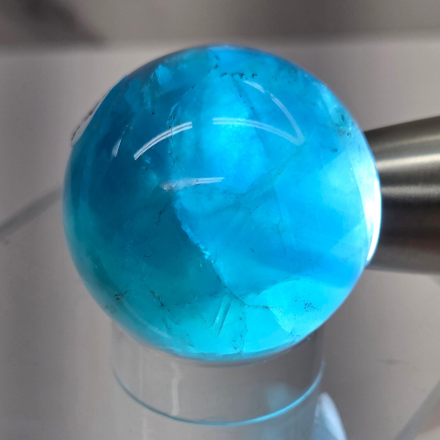 Backlit Blue Fluorite sphere on an acrylic stand against a white background