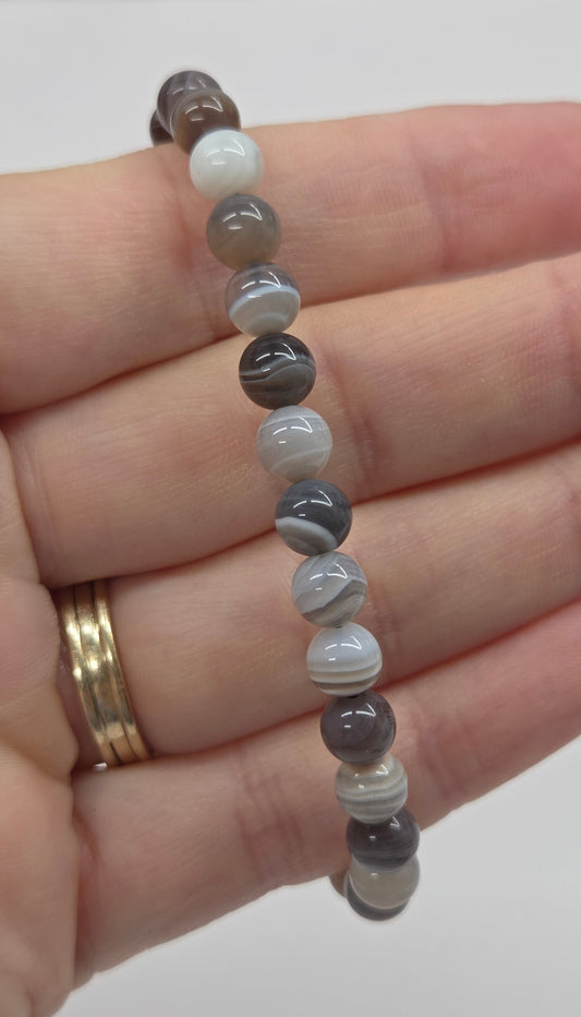 Banded agate beaded bracelet being held in a hand against a white background