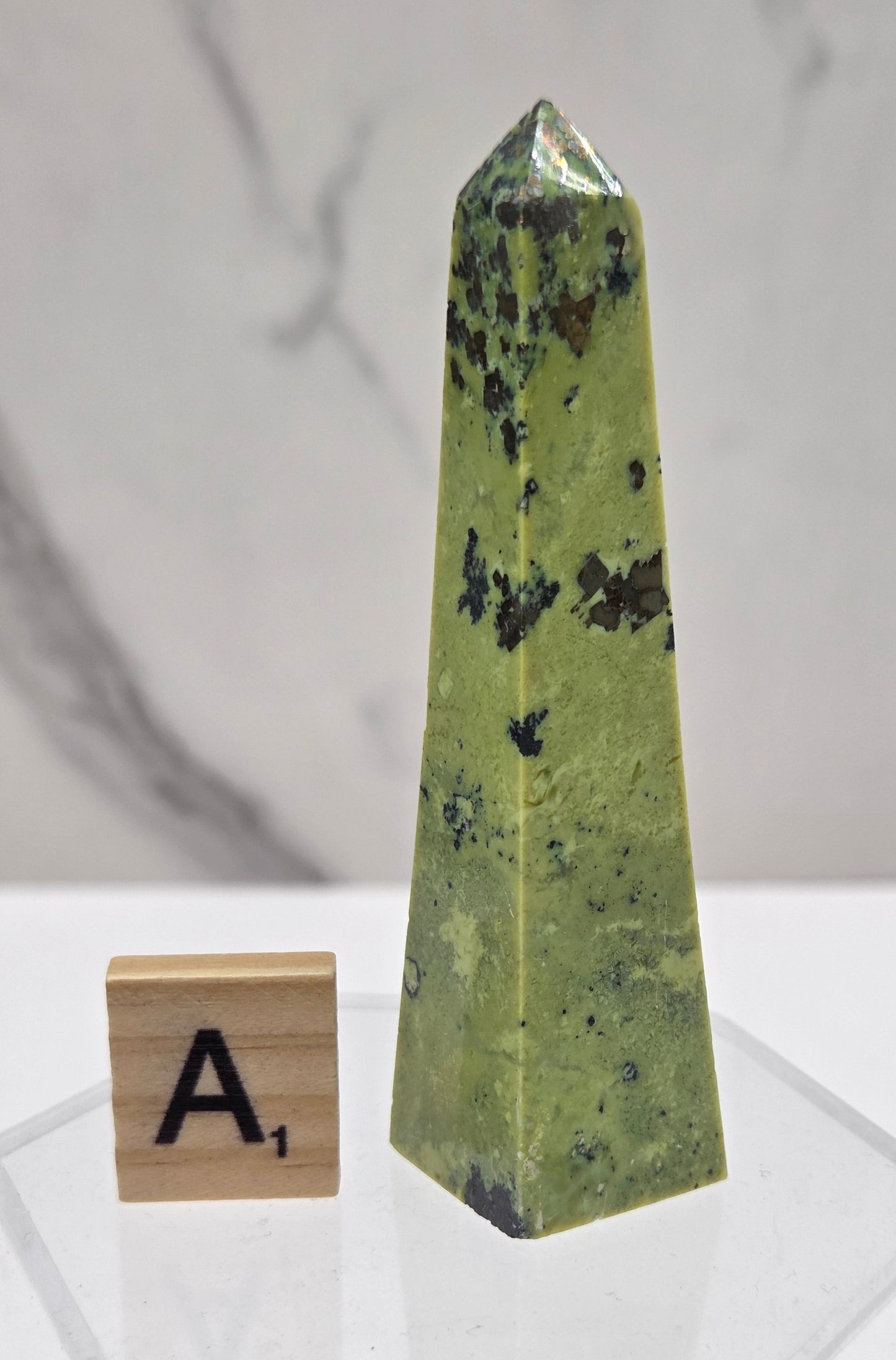 Green and brown crystal tower on an acrylic stand against a white background