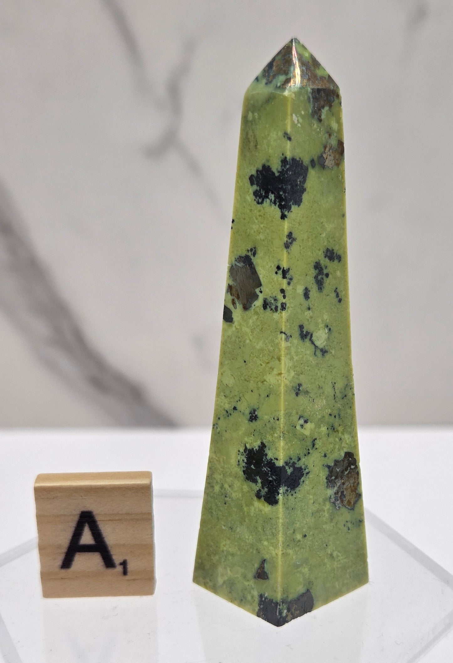 Green and brown crystal tower on an acrylic stand against a white background