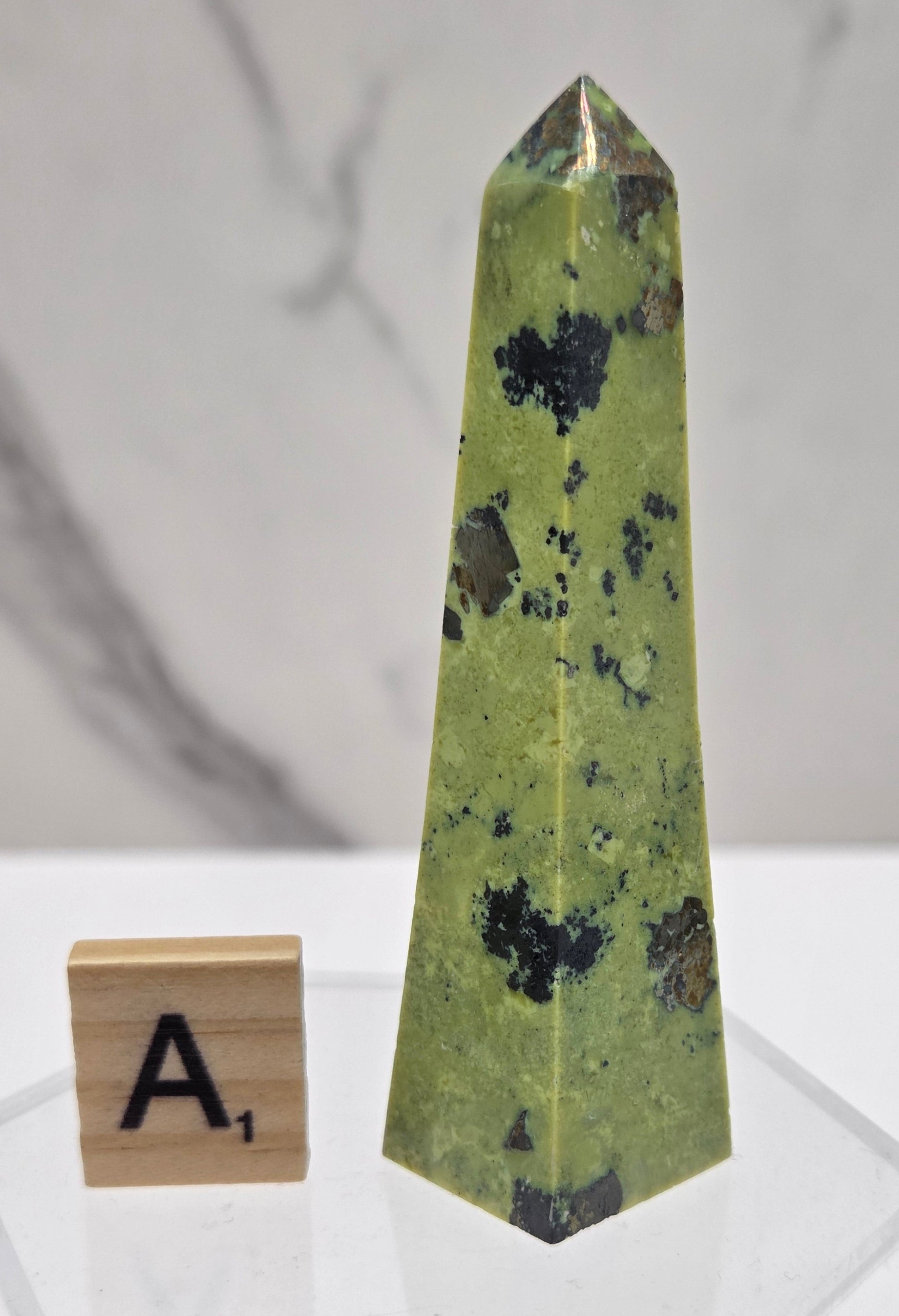 Green and brown crystal tower on an acrylic stand against a white background