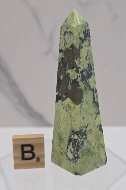 Green and brown crystal tower on an acrylic stand against a white background