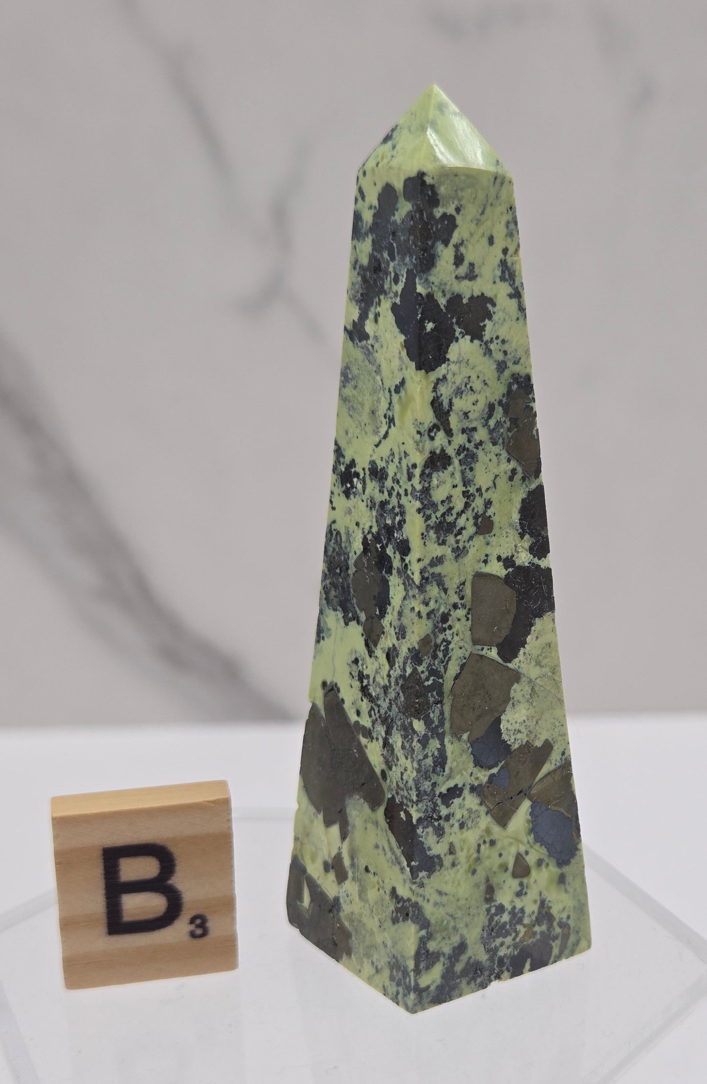 Green and brown crystal tower on an acrylic stand against a white background