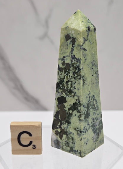 Green and brown crystal tower on an acrylic stand against a white background