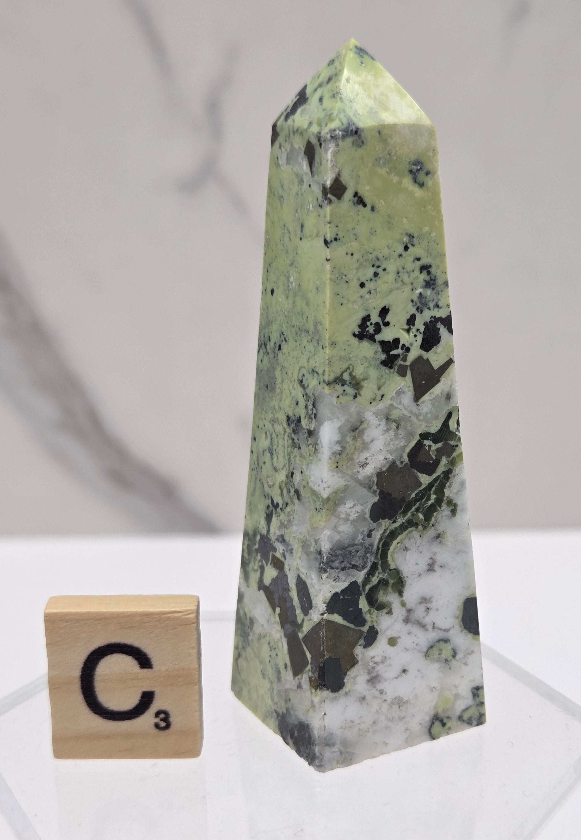 Green and brown crystal tower on an acrylic stand against a white background