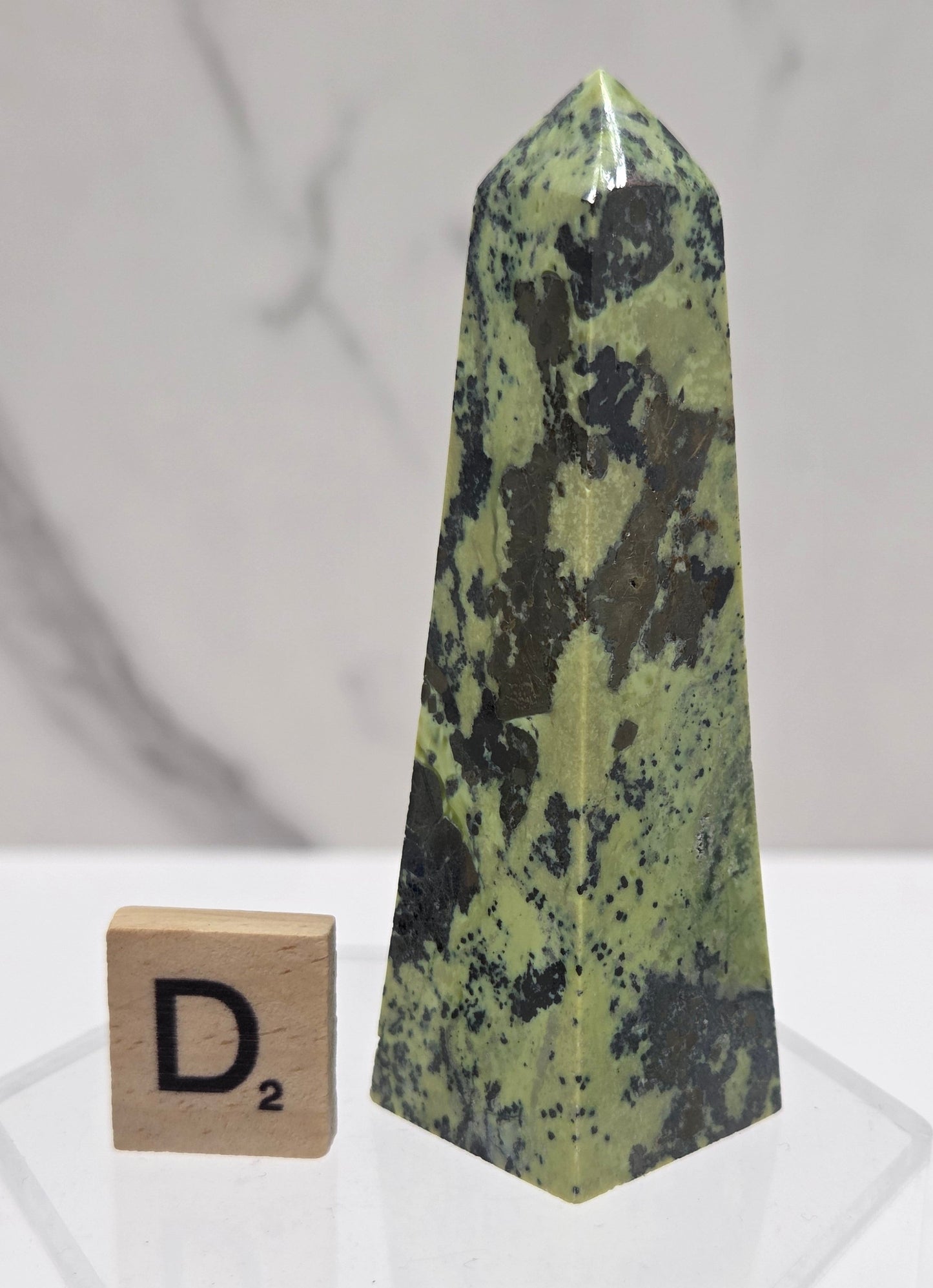 Green and brown crystal tower on an acrylic stand against a white background