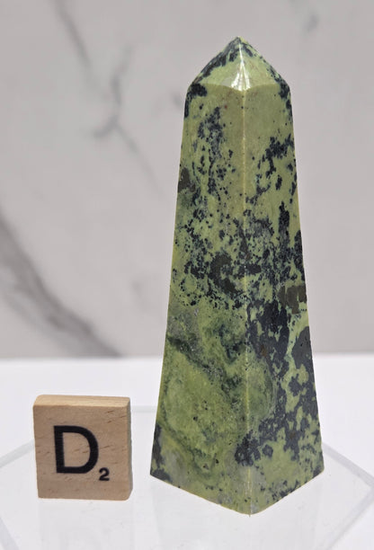 Green and brown crystal tower on an acrylic stand against a white background