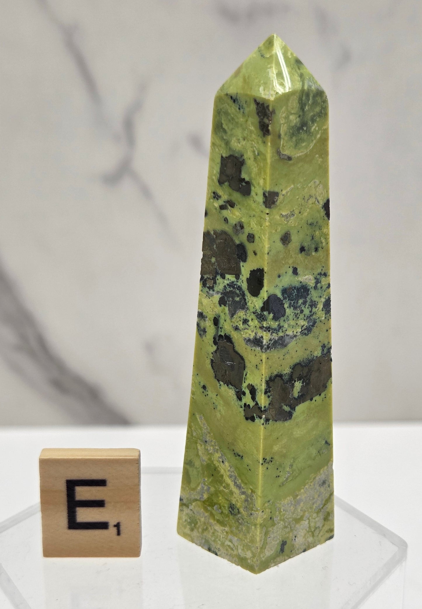 Green and brown crystal tower on an acrylic stand against a white background