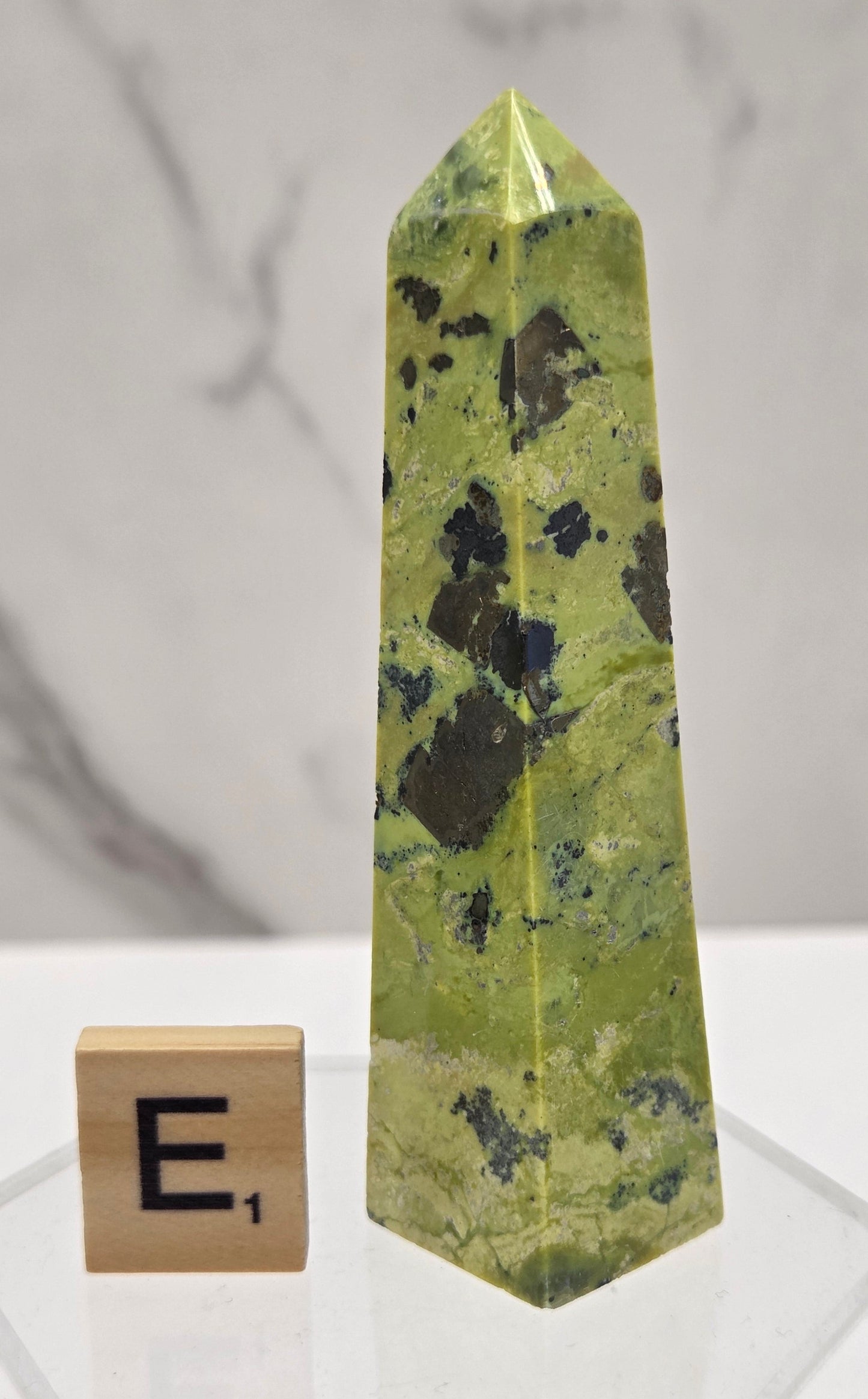 Green and brown crystal tower on an acrylic stand against a white background