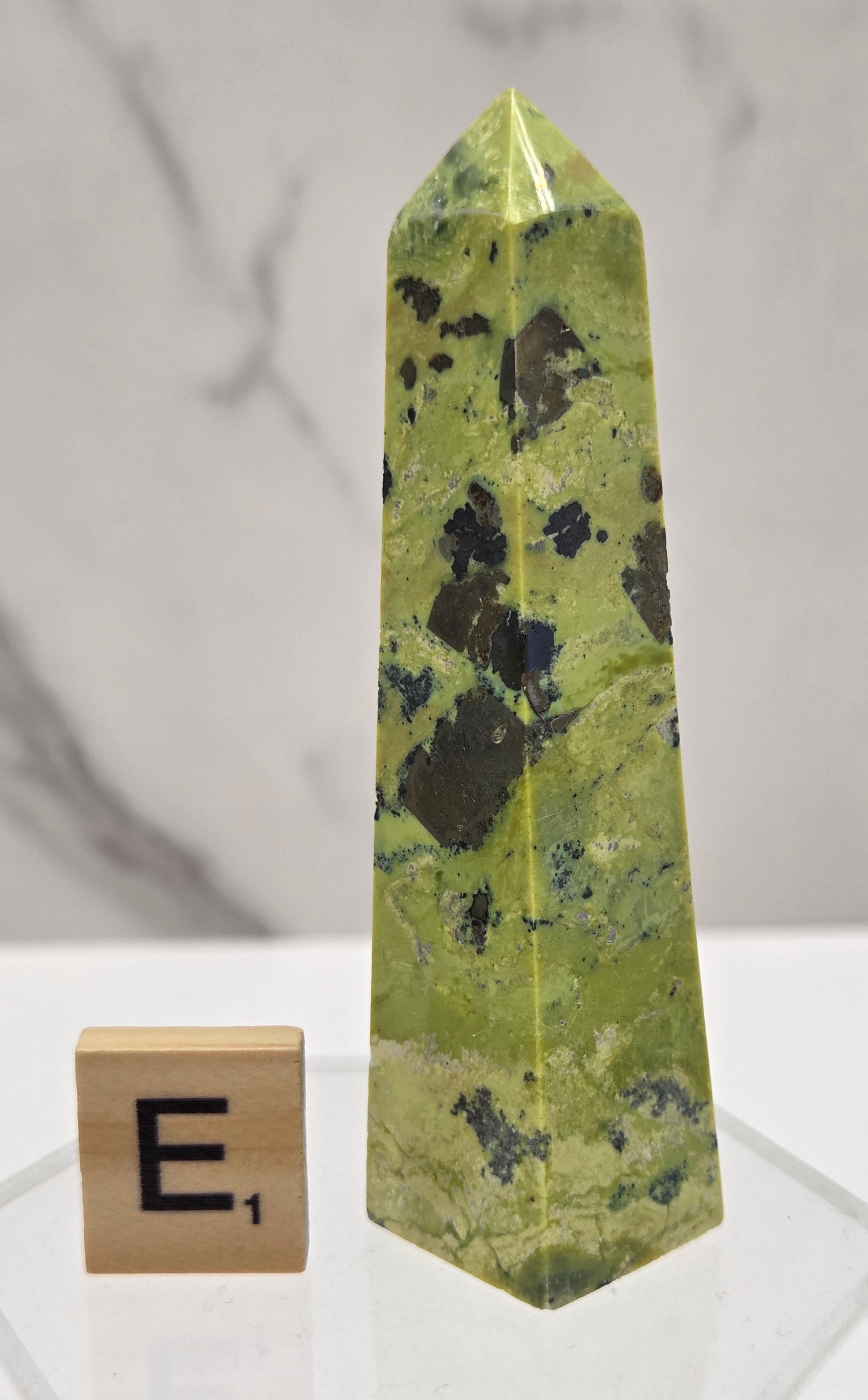 Green and brown crystal tower on an acrylic stand against a white background