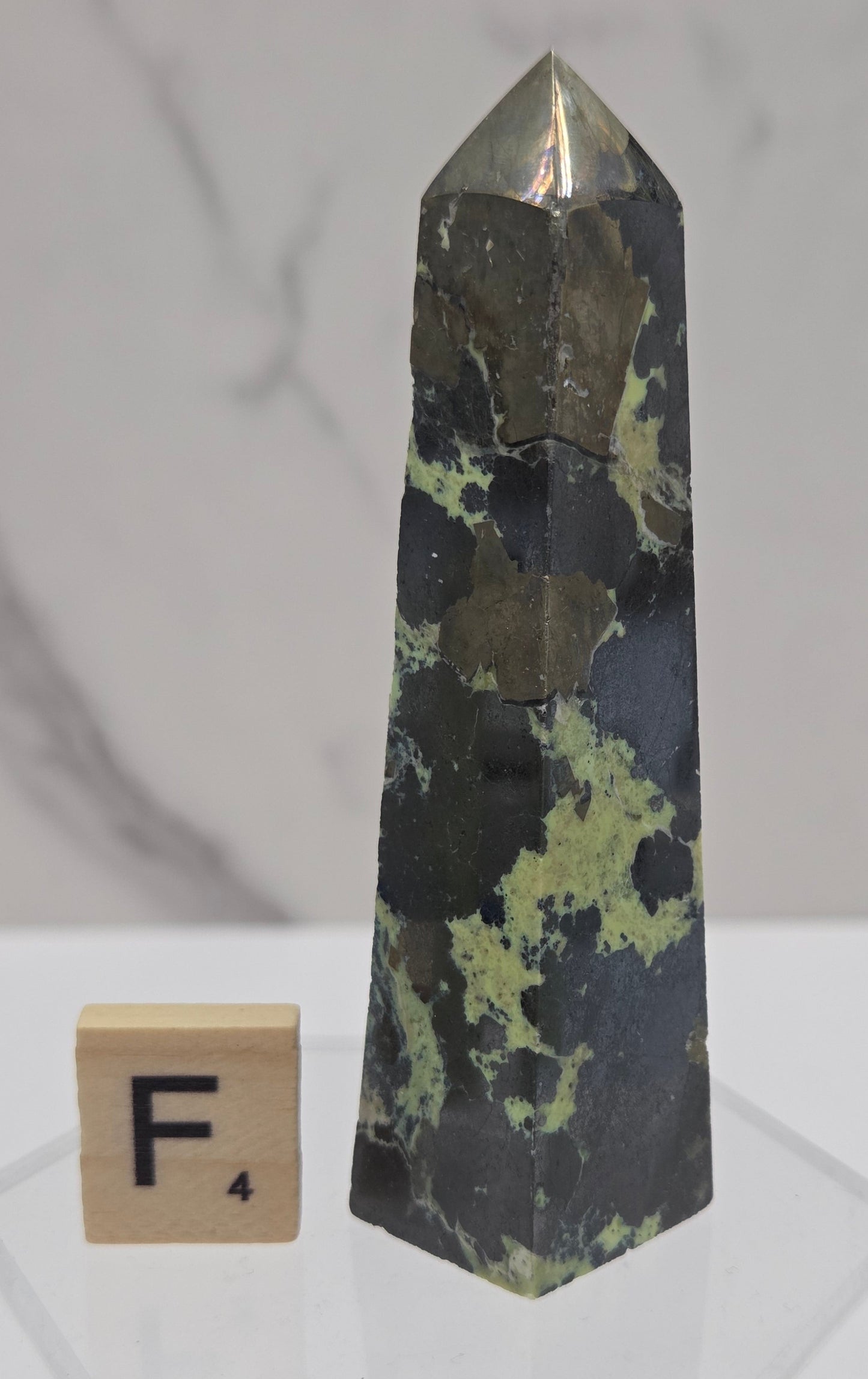 Green and brown crystal tower on an acrylic stand against a white background