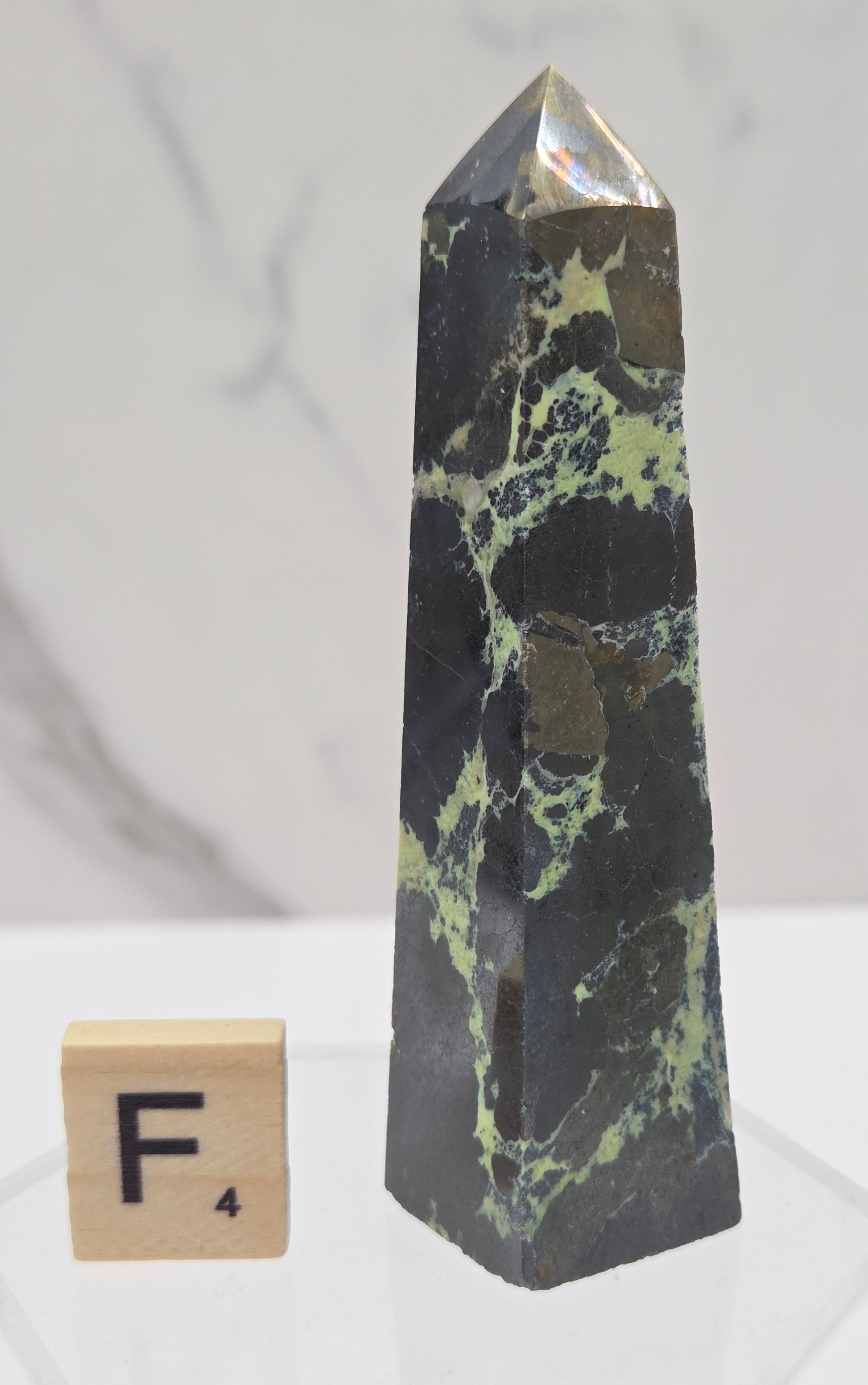 Green and brown crystal tower on an acrylic stand against a white background