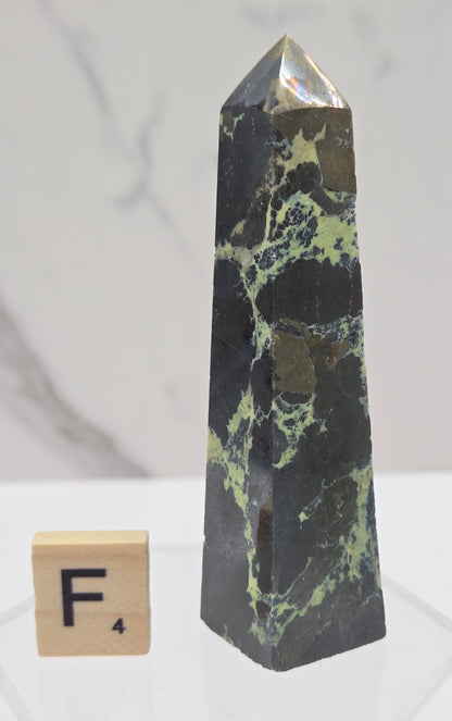 Green and brown crystal tower on an acrylic stand against a white background