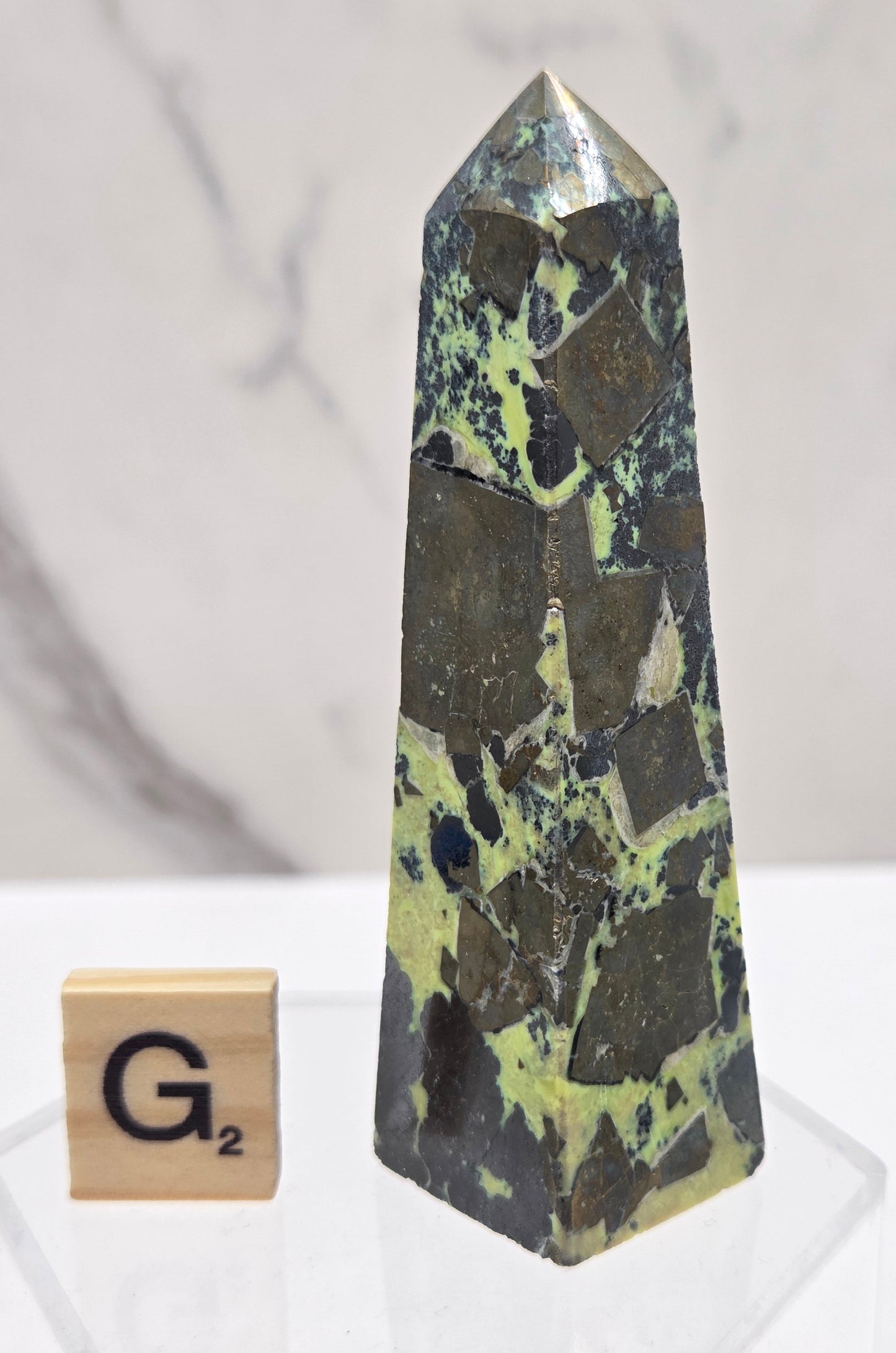 Green and brown crystal tower on an acrylic stand against a white background