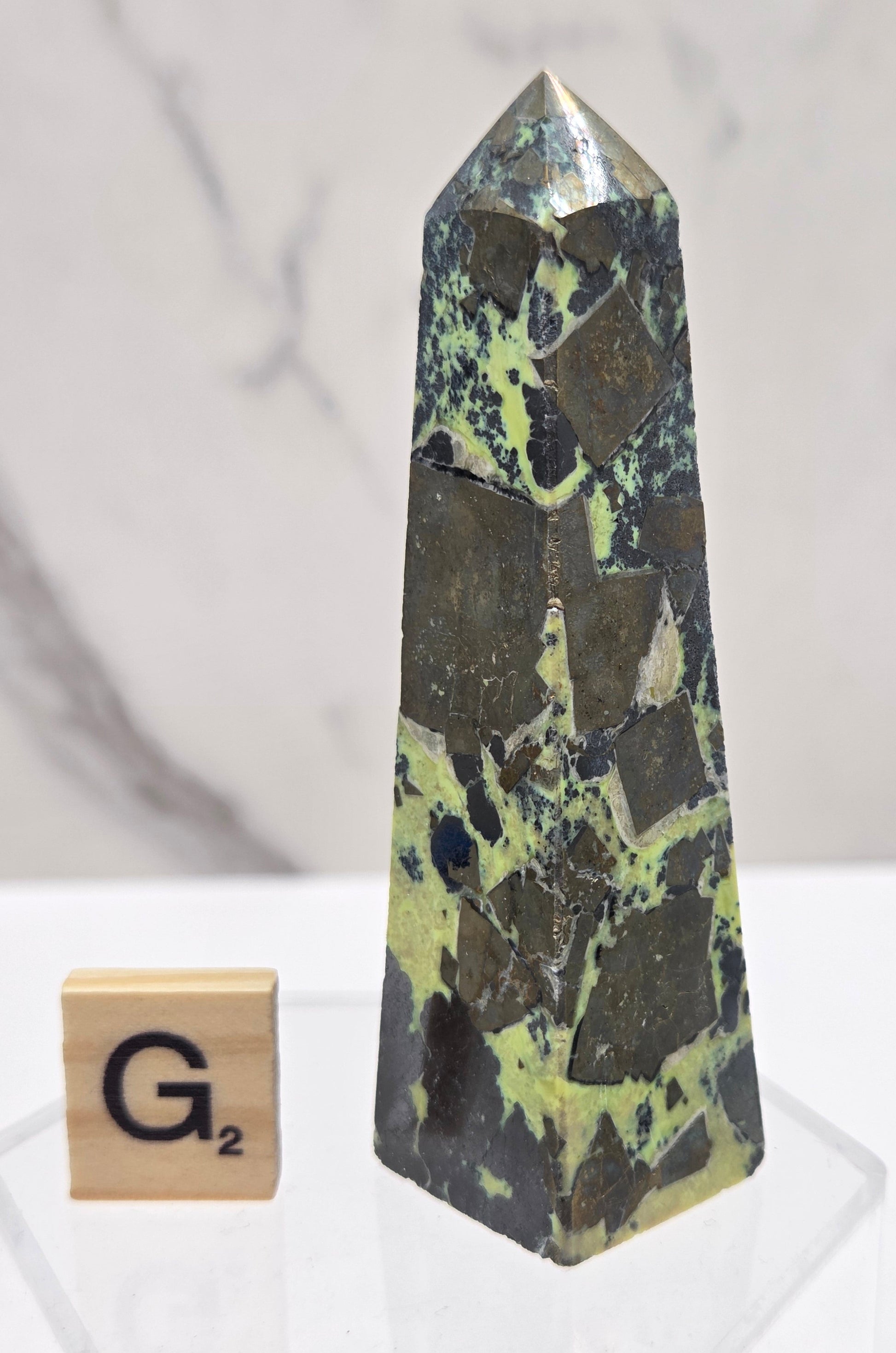 Green and brown crystal tower on an acrylic stand against a white background