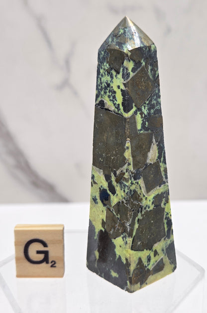 Green and brown crystal tower on an acrylic stand against a white background