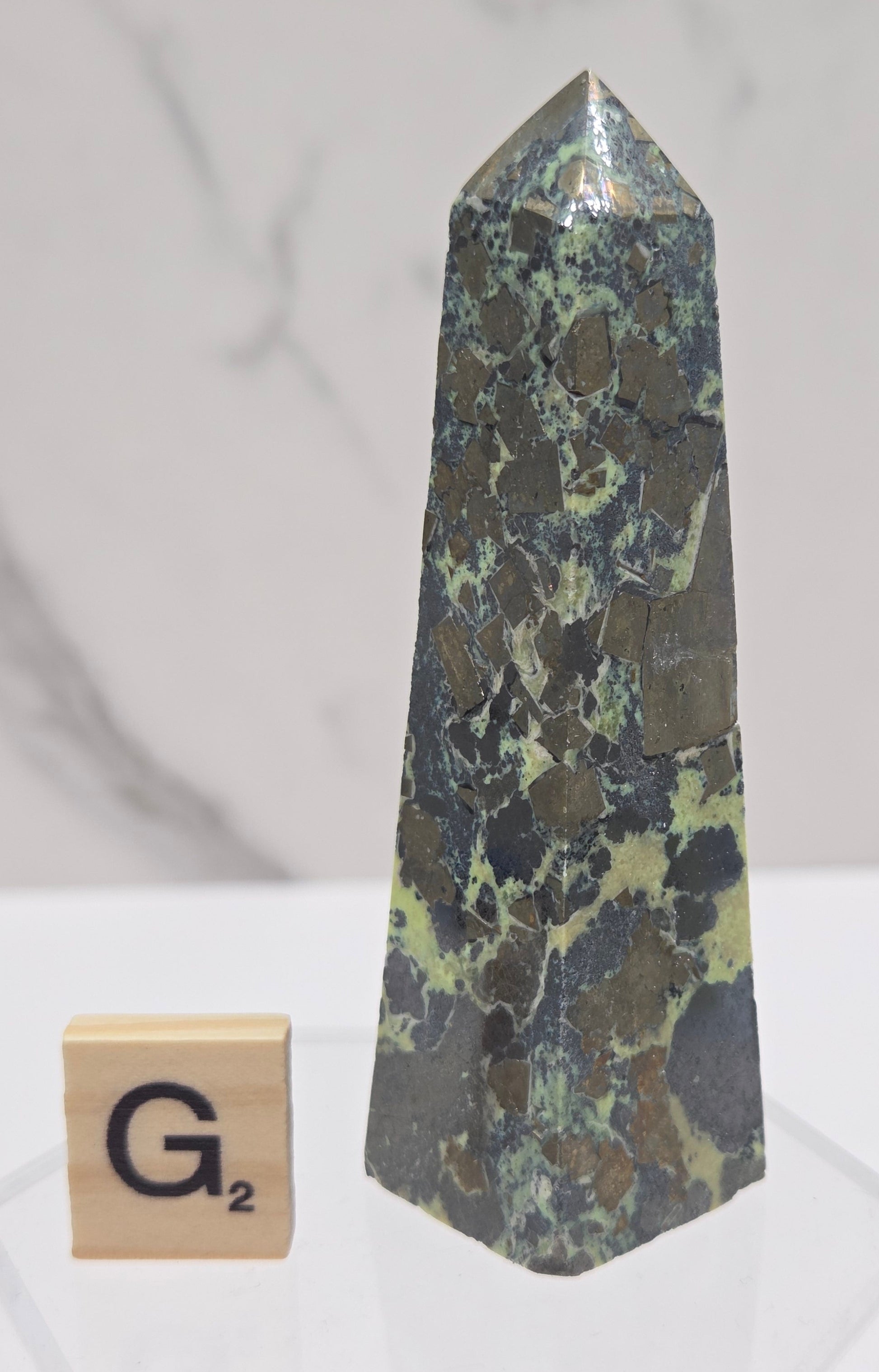 Green and brown crystal tower on an acrylic stand against a white background