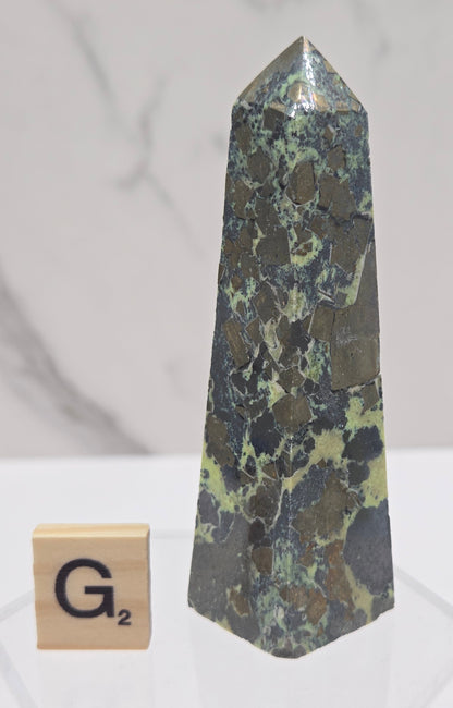 Green and brown crystal tower on an acrylic stand against a white background