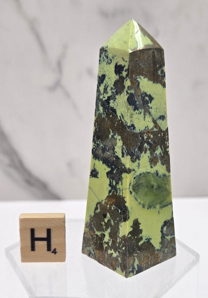 Green and brown crystal tower on an acrylic stand against a white background