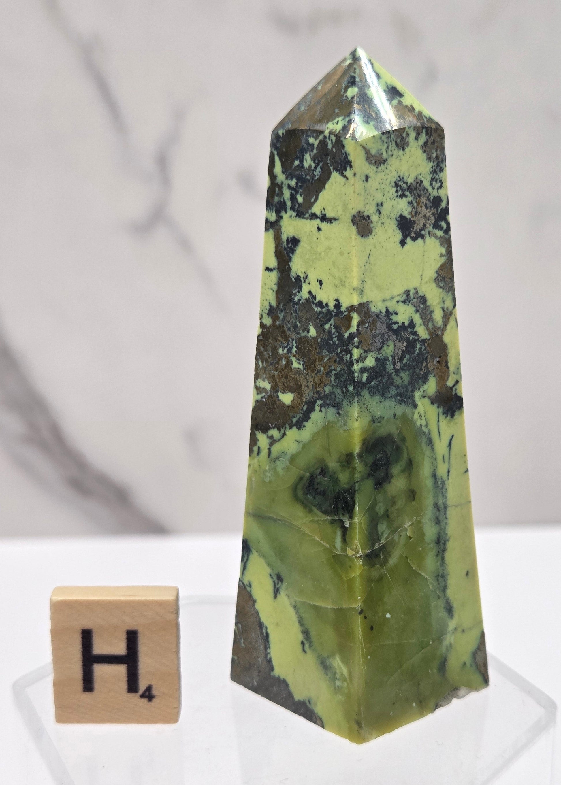 Green and brown crystal tower on an acrylic stand against a white background