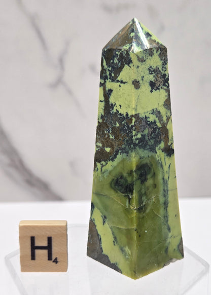 Green and brown crystal tower on an acrylic stand against a white background