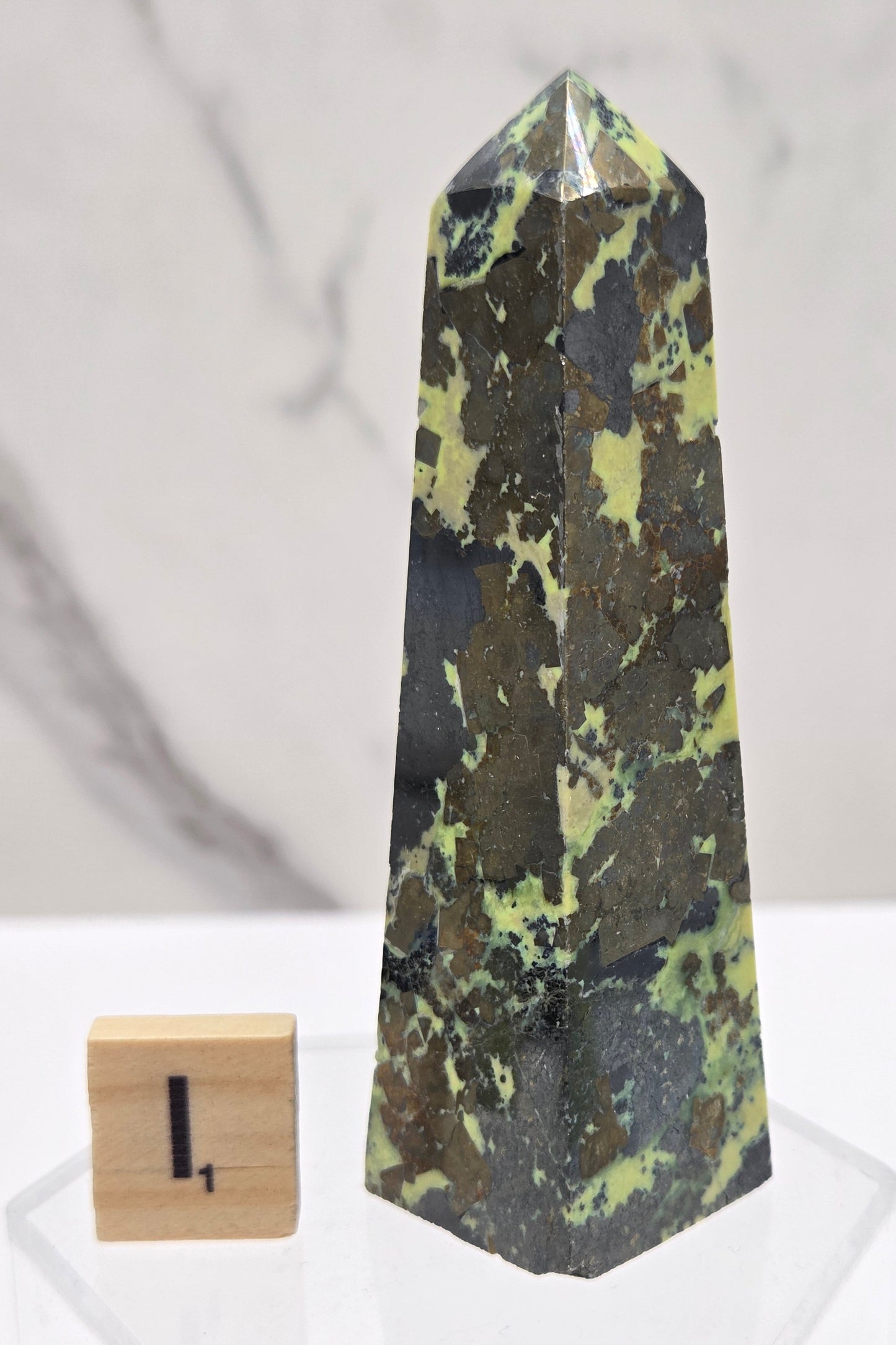 Green and brown crystal tower on an acrylic stand against a white background