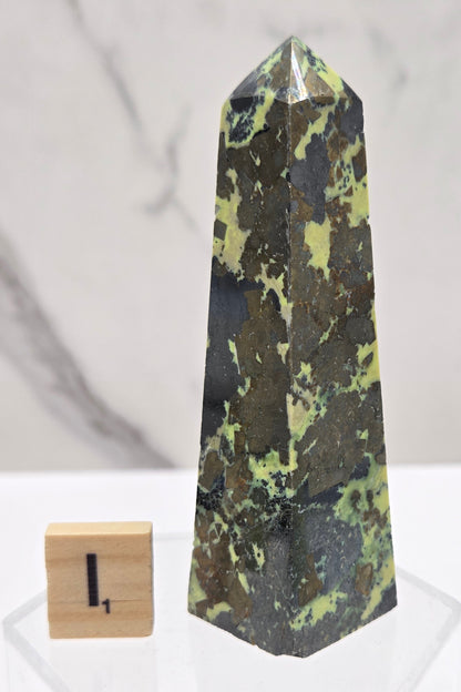 Green and brown crystal tower on an acrylic stand against a white background