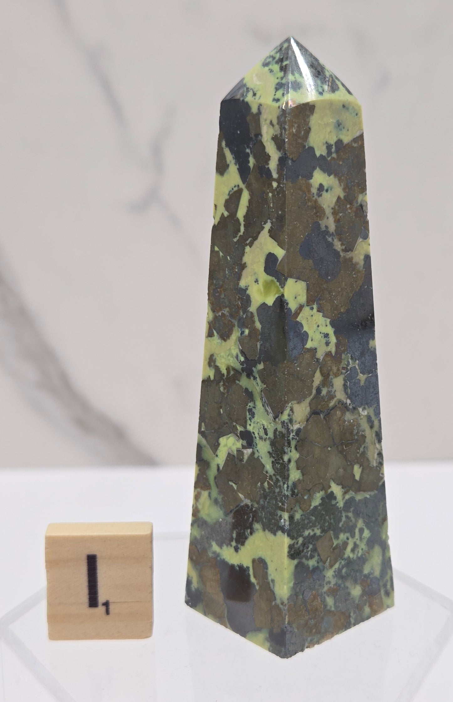 Green and brown crystal tower on an acrylic stand against a white background