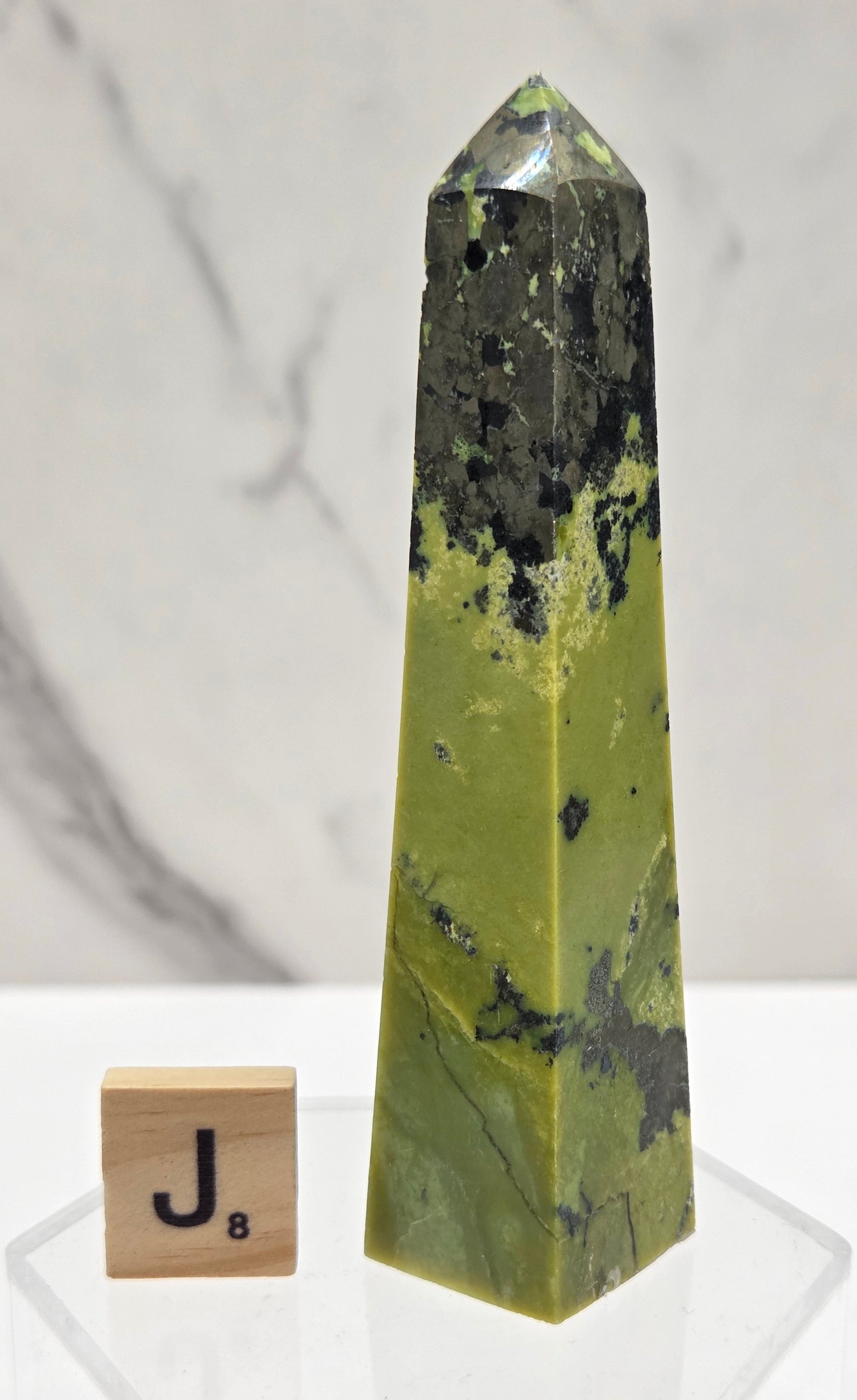 Green and brown crystal tower on an acrylic stand against a white background