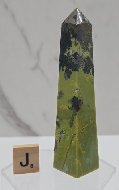 Green and brown crystal tower on an acrylic stand against a white background