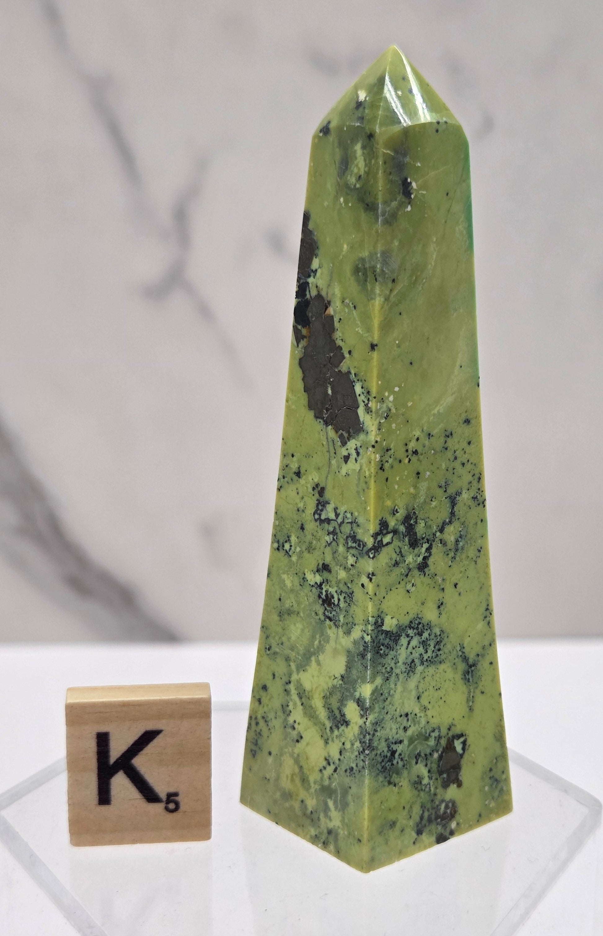 Green and brown crystal tower on an acrylic stand against a white background