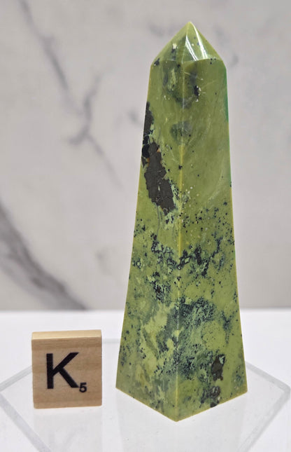 Green and brown crystal tower on an acrylic stand against a white background