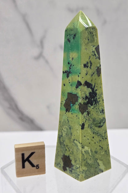 Green and brown crystal tower on an acrylic stand against a white background