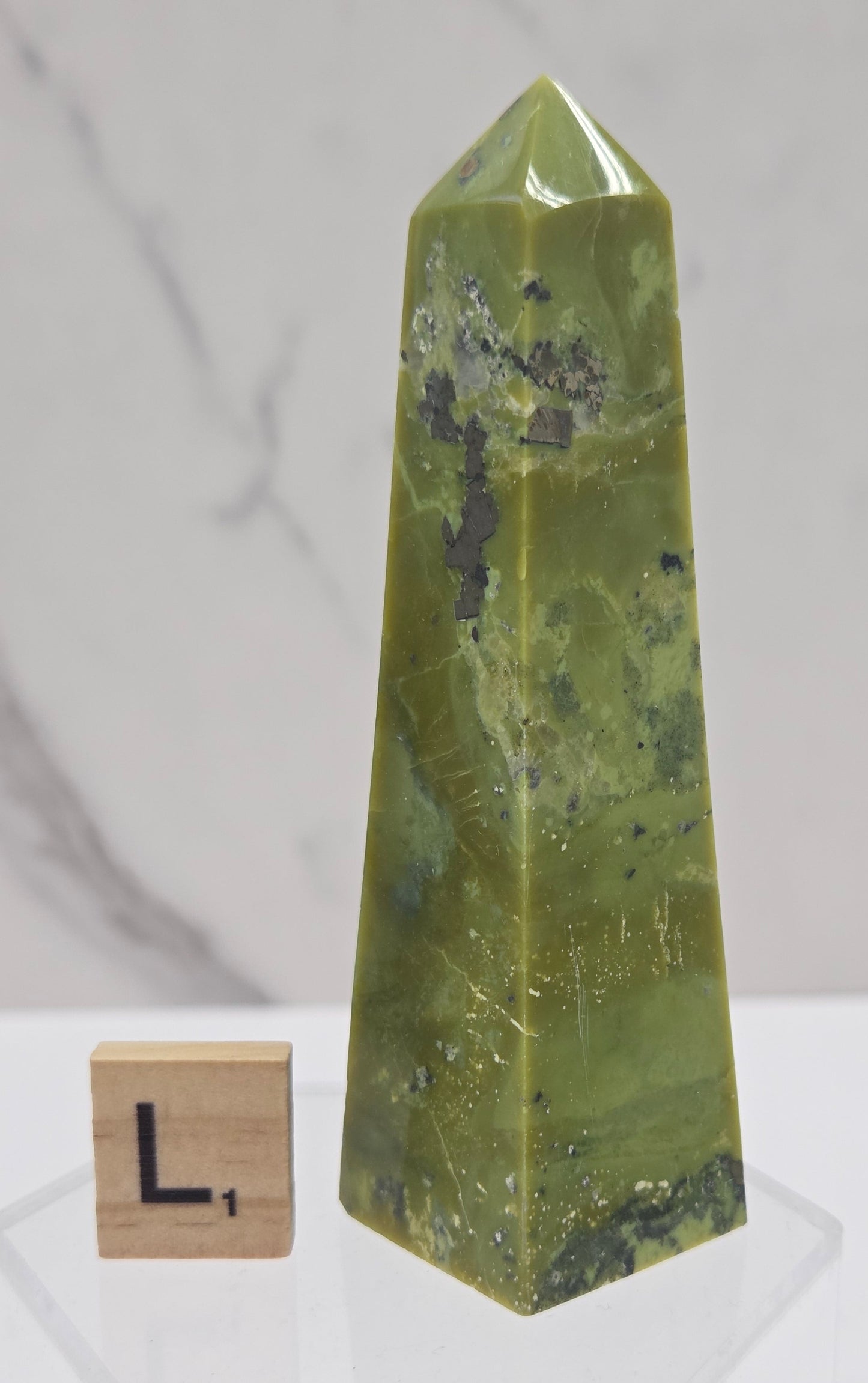 Green and brown crystal tower on an acrylic stand against a white background