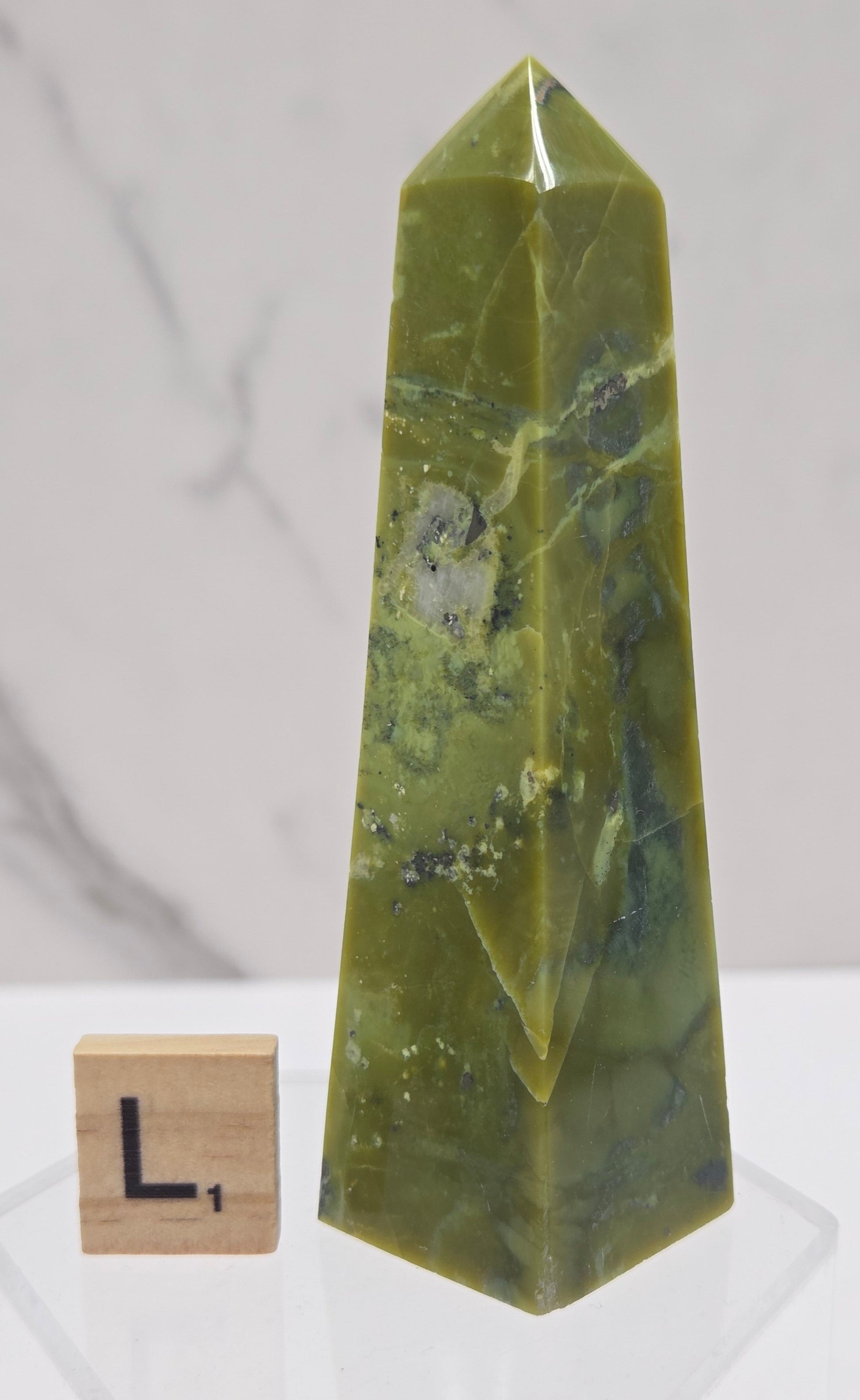 Green and brown crystal tower on an acrylic stand against a white background