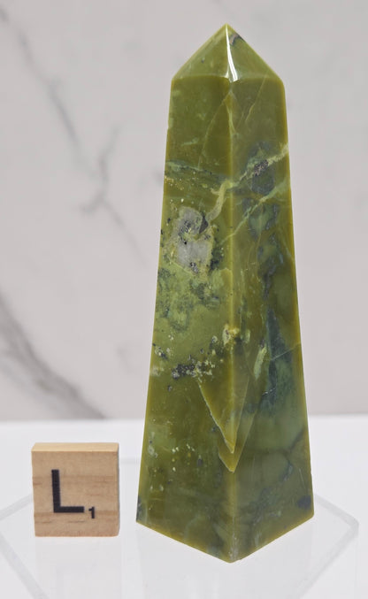 Green and brown crystal tower on an acrylic stand against a white background