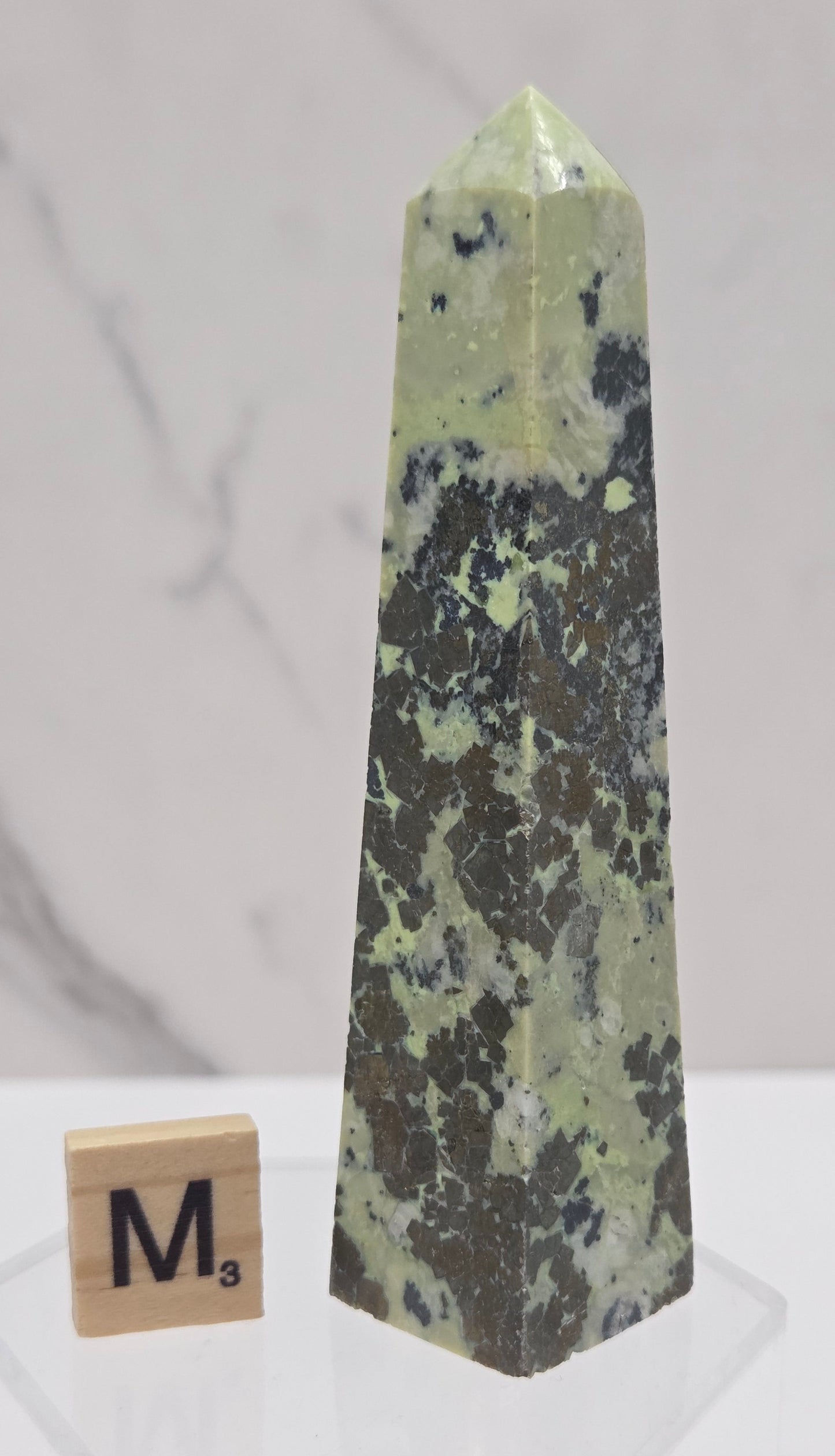 Green and brown crystal tower on an acrylic stand against a white background