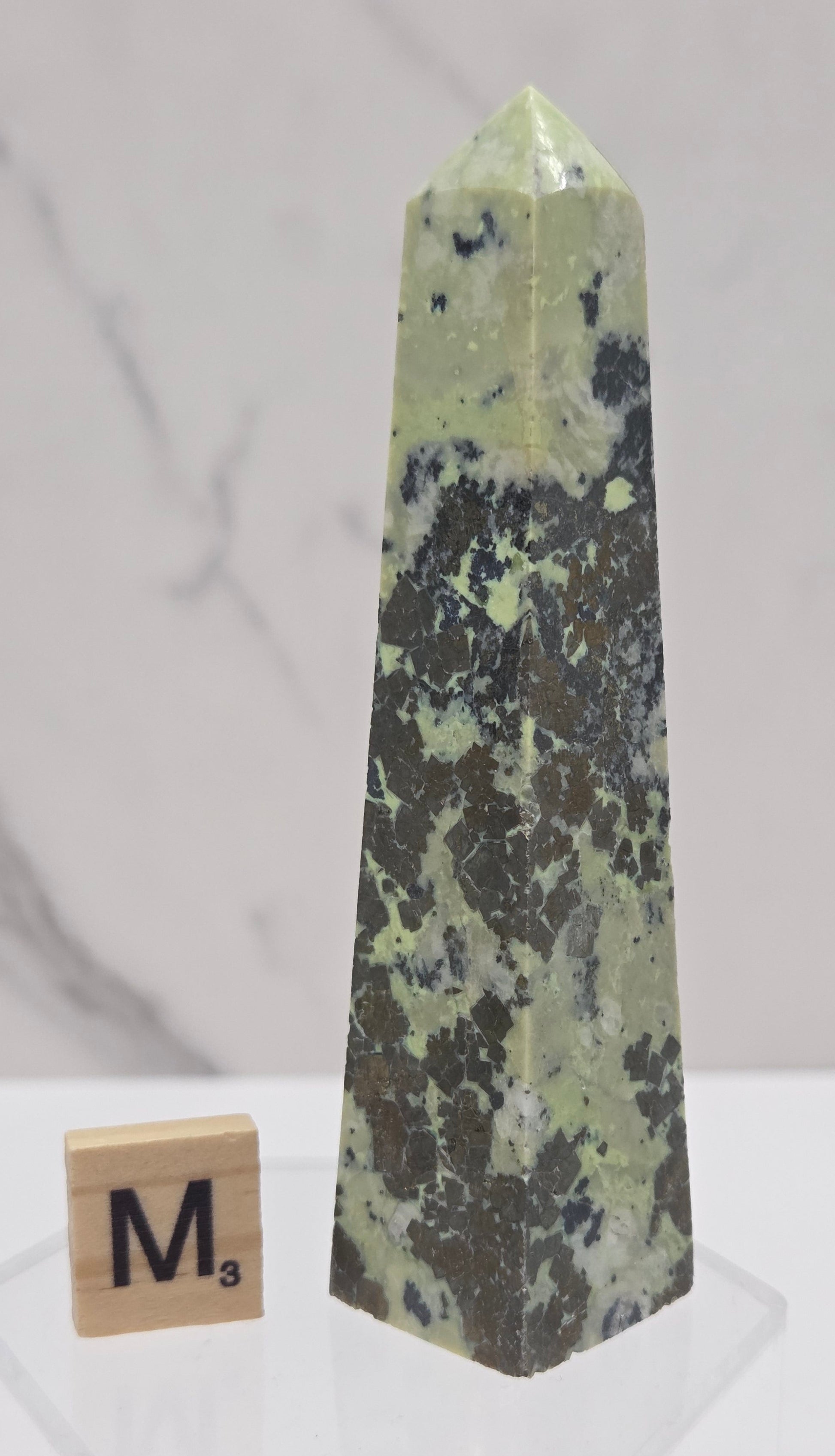 Green and brown crystal tower on an acrylic stand against a white background