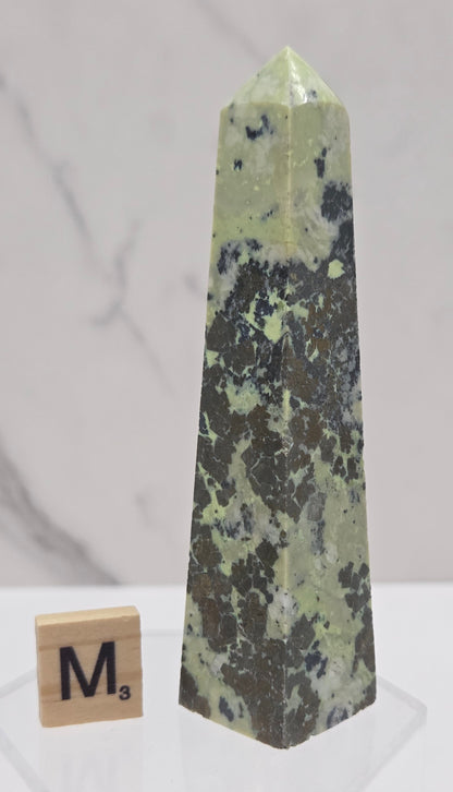 Green and brown crystal tower on an acrylic stand against a white background