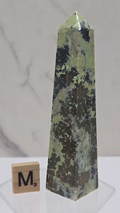 Green and brown crystal tower on an acrylic stand against a white background