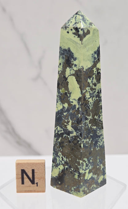Green and brown crystal tower on an acrylic stand against a white background