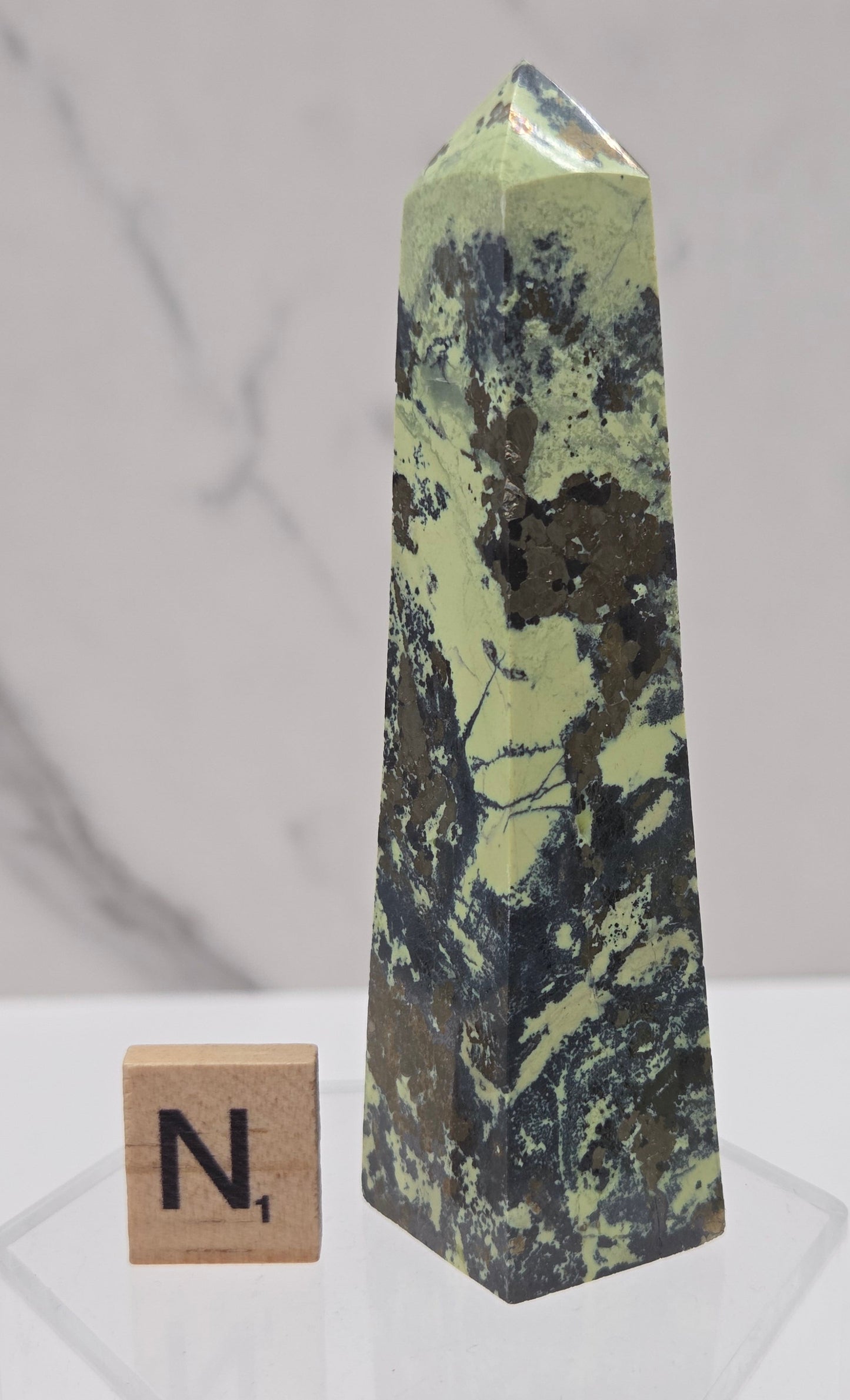 Green and brown crystal tower on an acrylic stand against a white background