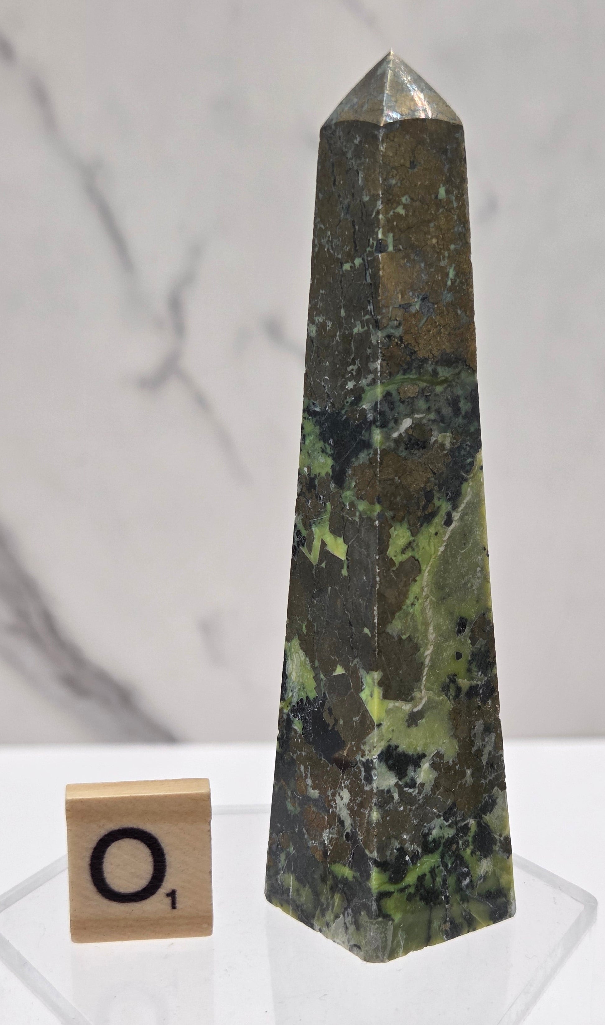 Green and brown crystal tower on an acrylic stand against a white background