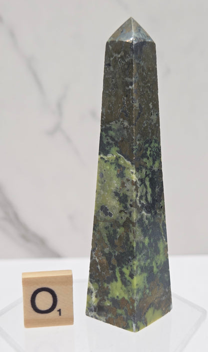 Green and brown crystal tower on an acrylic stand against a white background