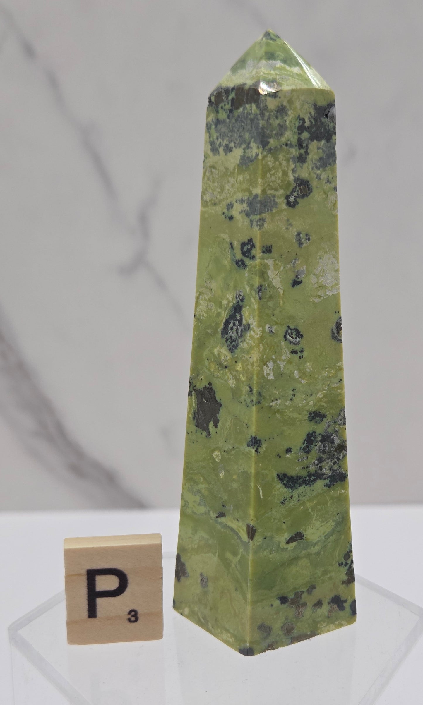 Green and brown crystal tower on an acrylic stand against a white background