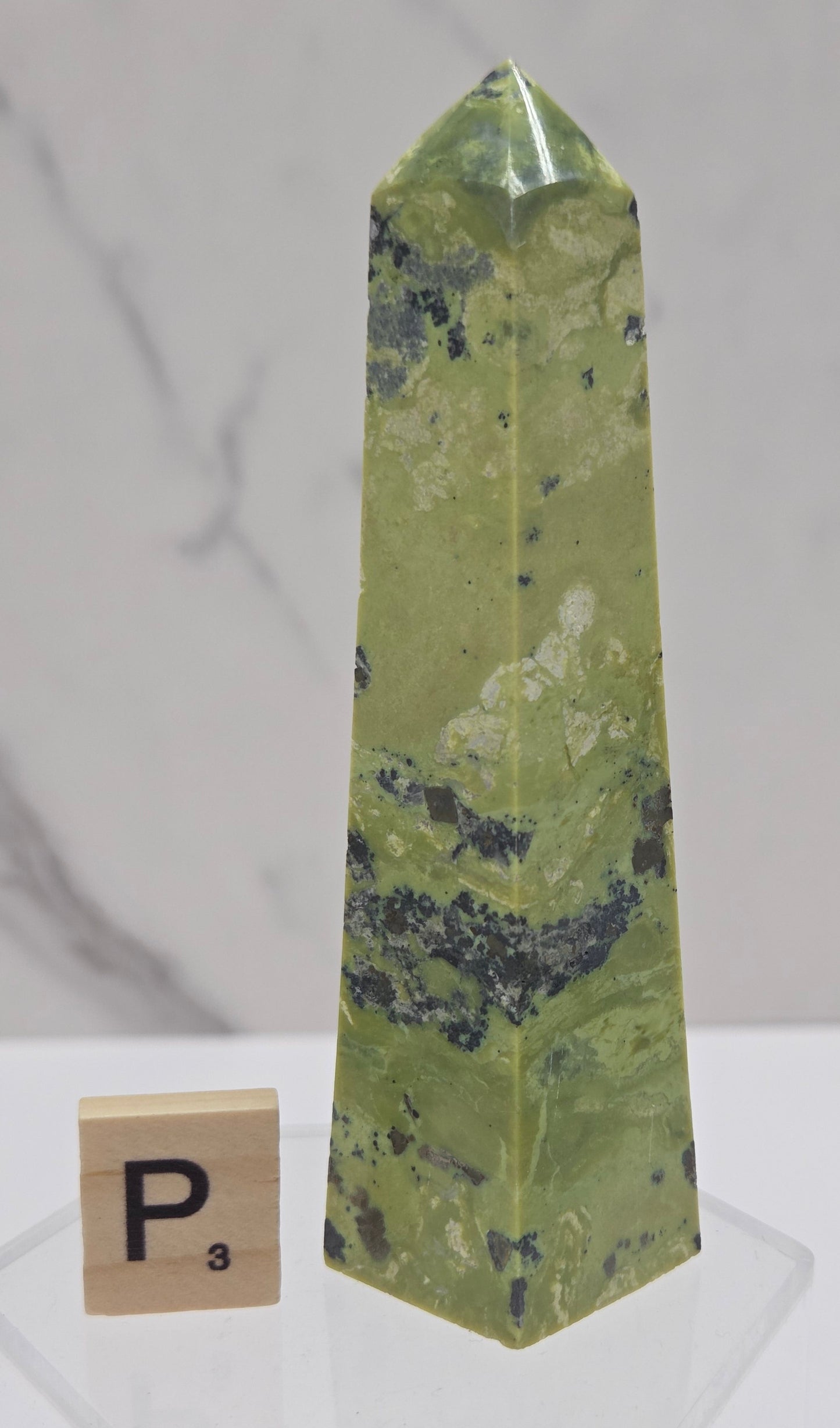 Green and brown crystal tower on an acrylic stand against a white background