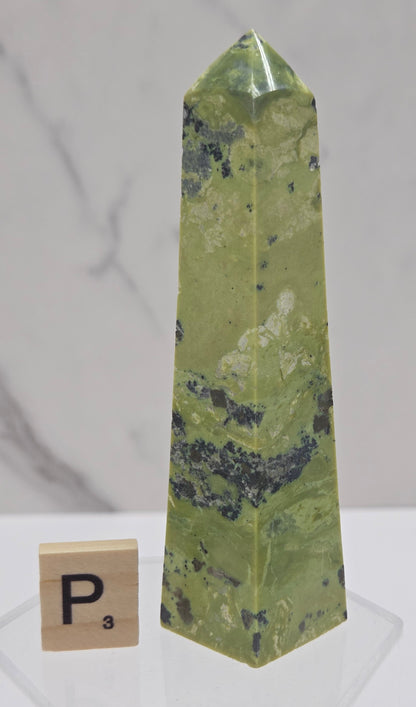 Green and brown crystal tower on an acrylic stand against a white background